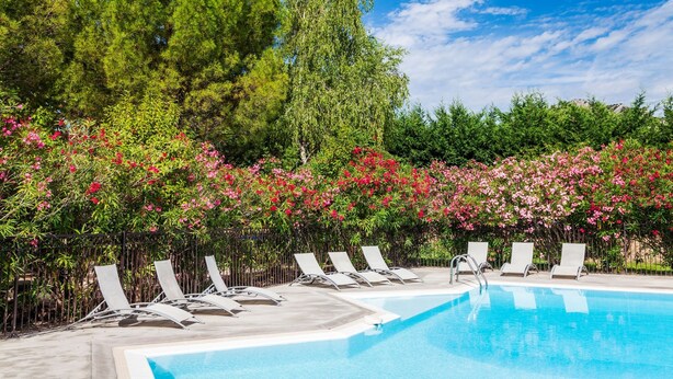 Una piscina con sillones de descanso y un jardín exuberante con arbustos florecientes.