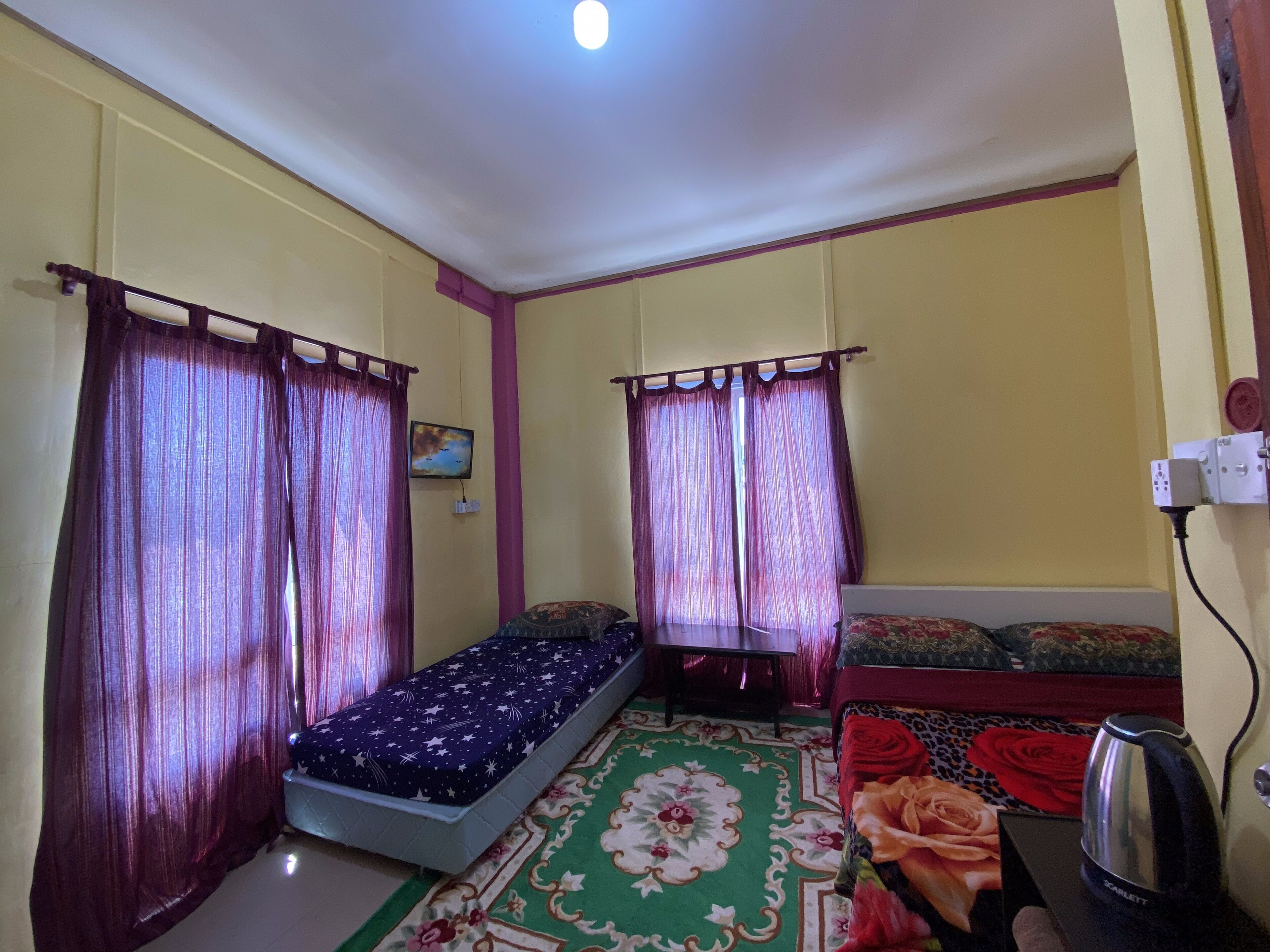 Una habitación pequeña y luminosa con dos camas individuales, un sofá, un tapete estampado y una tetera sobre una mesa.