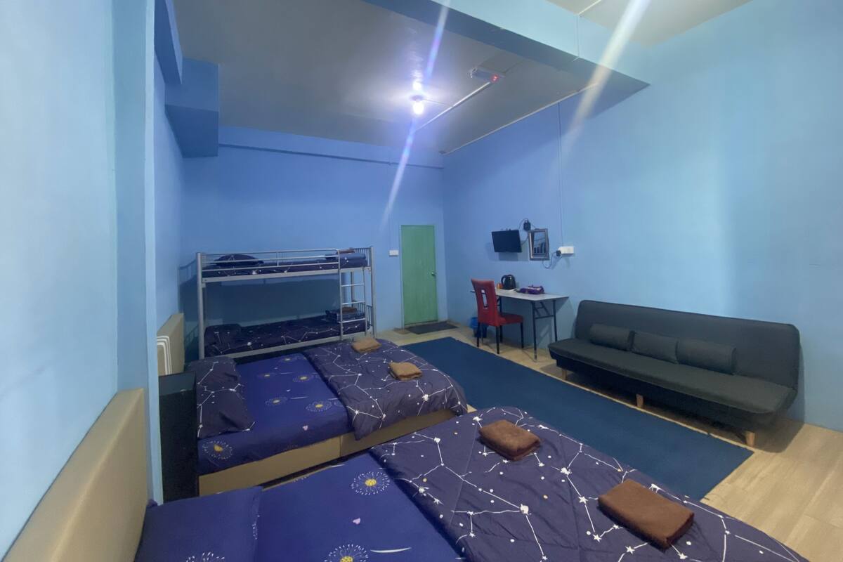 A dormitory room with bunk beds, a desk, a chair, a couch, and a TV on the wall.