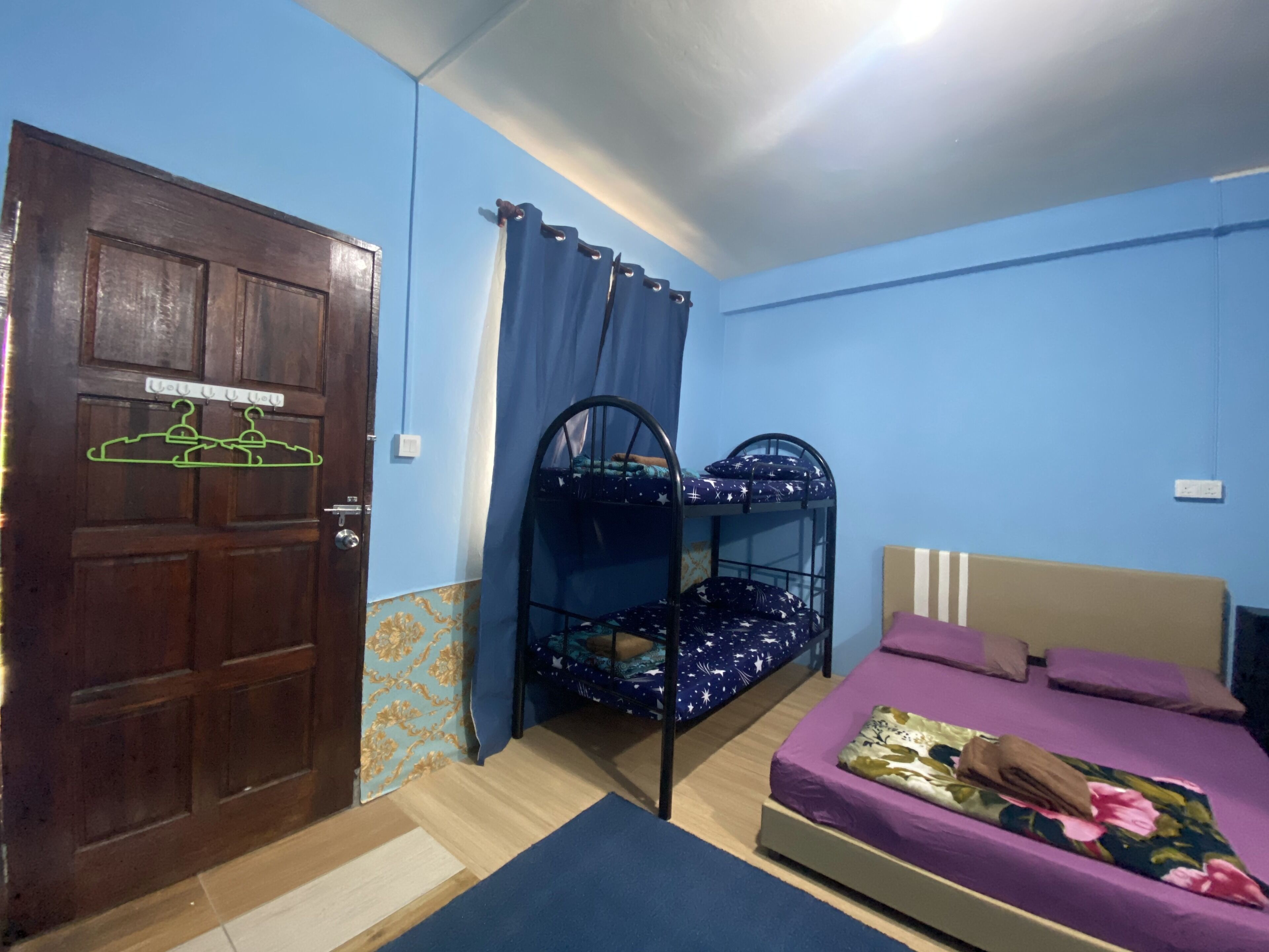 Una habitación con literas, una cama individual, una puerta de madera y una cortina.