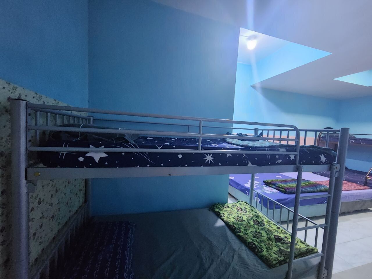 Una cama litera con colchón estampado de estrellas, una cama inferior con manta verde estampada y una pared azul.