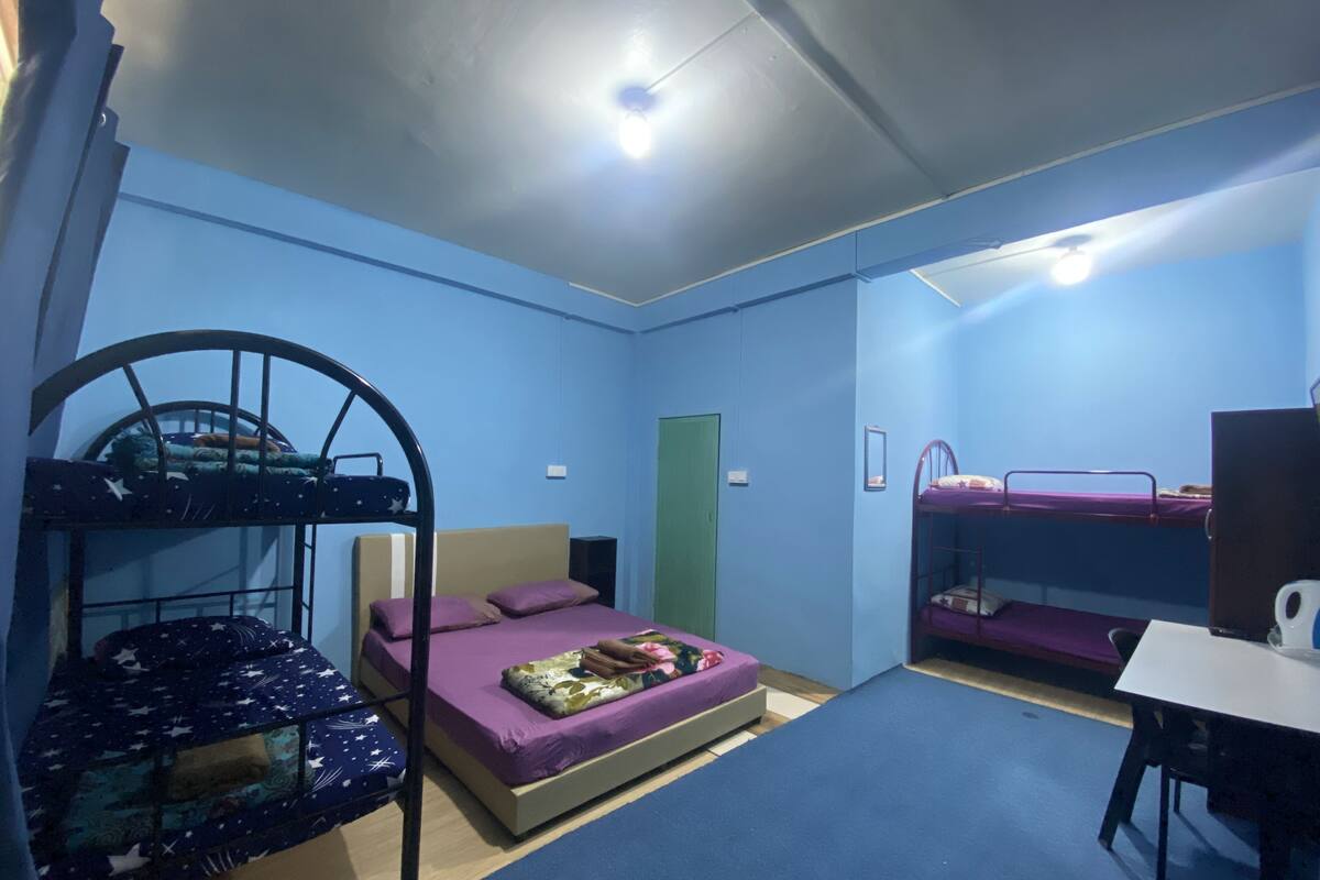 A dormitory room with bunk beds, a desk, and a green door.