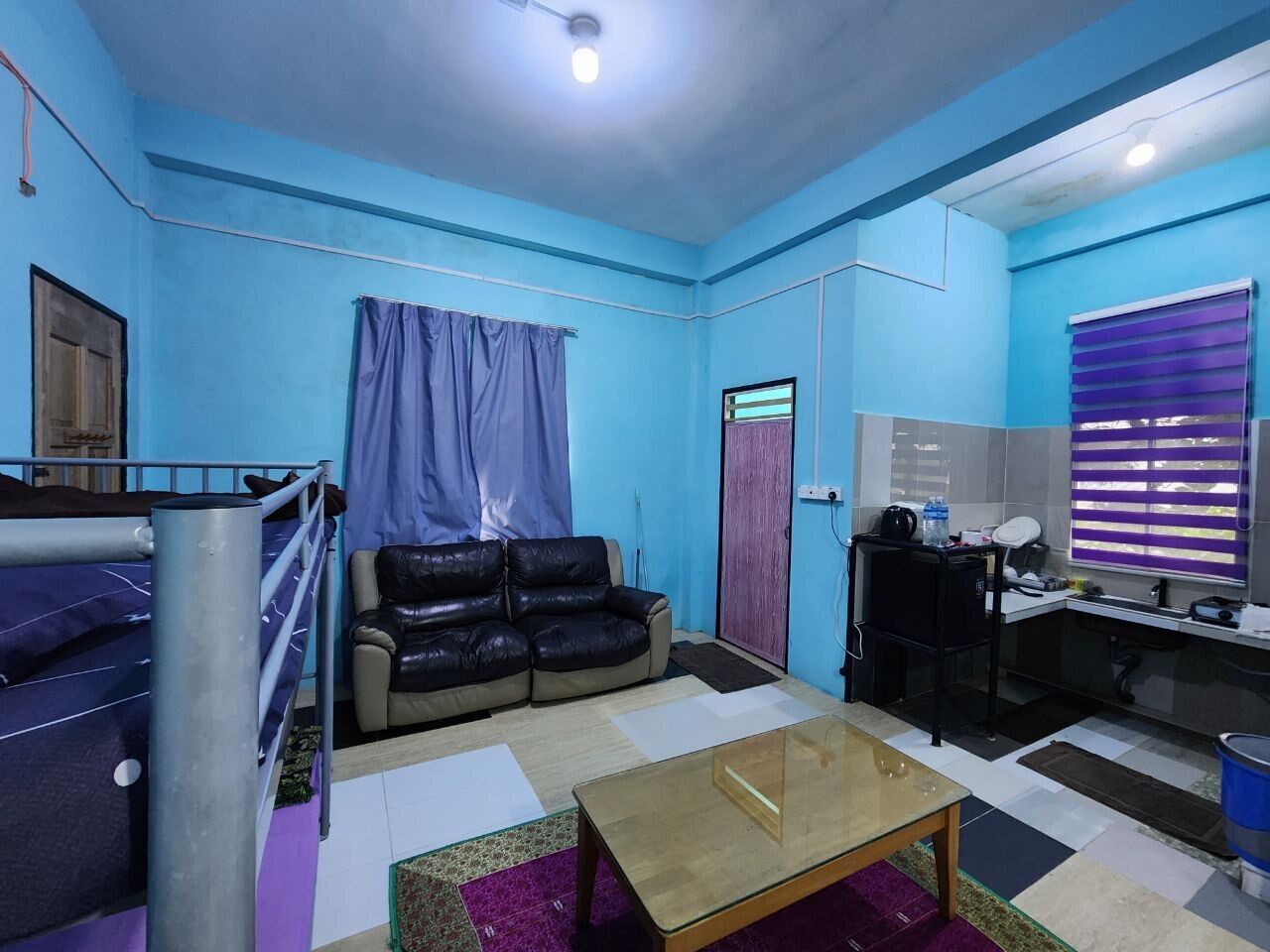 A room with a bunk bed, a sofa, a desk, and a window with blinds.