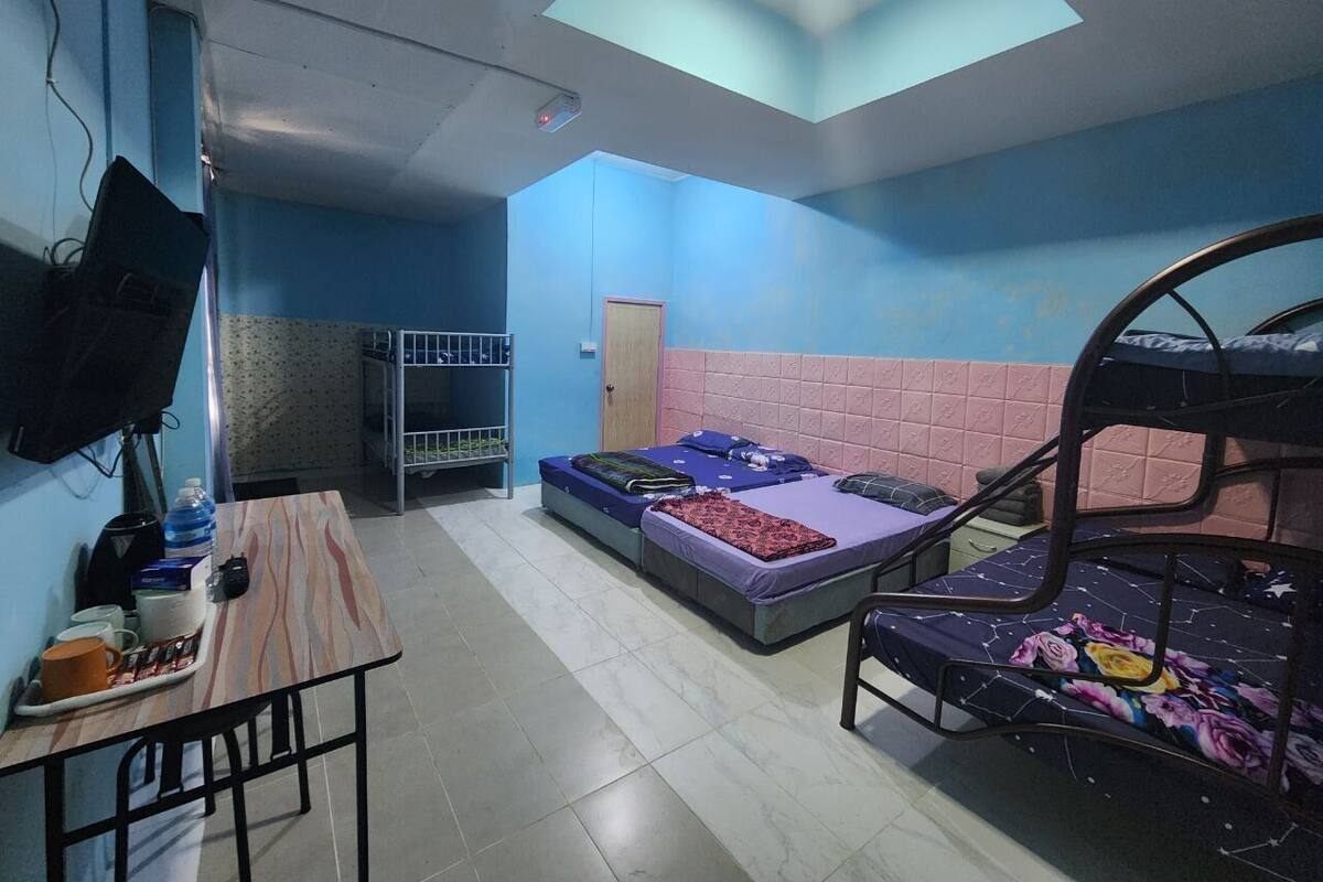 A dormitory room with two bunk beds, a desk with a chair, a television, and a window with a skylight.