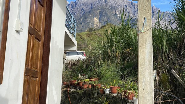 A view of a mountain range through a doorway, with a white building and a wooden door on the left. - Kupi-Kupi & Stay (Ranau)