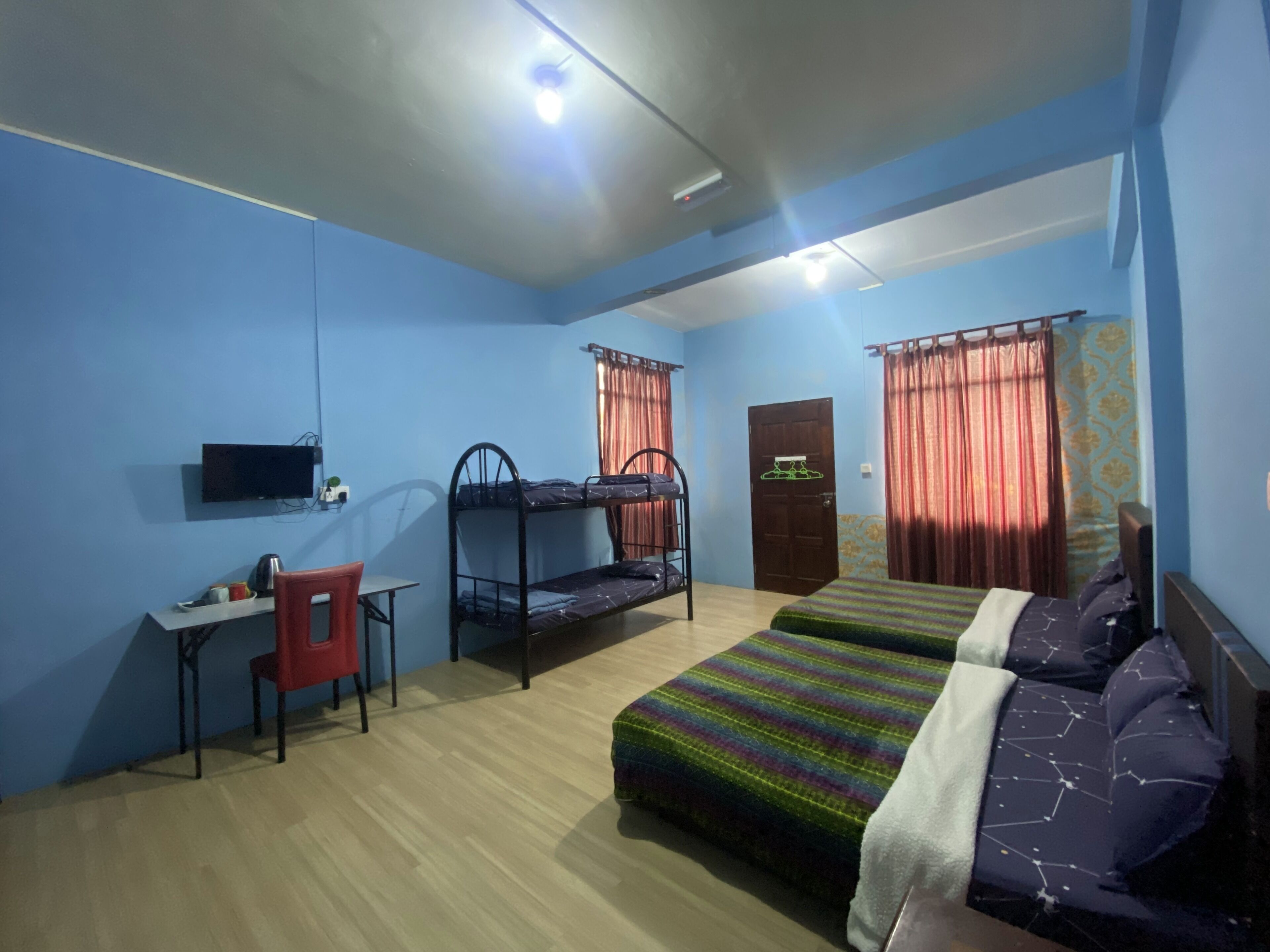 A dormitory room with bunk beds, a desk, a chair, and a television.