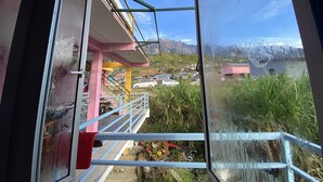 A view from a window with a metal frame, overlooking a balcony with potted plants and a red towel hanging on the railing. - Kupi-Kupi & Stay (Ranau)