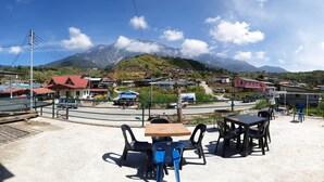 A patio with tables and chairs, overlooking a village and mountains. - Kupi-Kupi & Stay (Ranau)