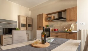 A modern kitchen with wooden cabinets, a dining table with a cork coaster, a bottle of wine, and a TV on a stand. - Manzoni Apartment (Roseto degli Abruzzi)