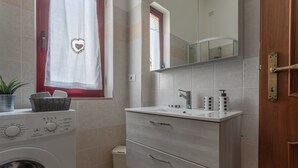 A bathroom with a washing machine, a sink with a mirror above it, and a wooden door. - Manzoni Apartment (Roseto degli Abruzzi)