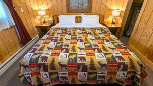 A hotel room with wooden paneling, a quilted bedspread with animal prints, two bedside lamps, and a framed picture on the wall. - Yellowstone's Treasure Cabin #6, few min drive from Yellowstone Park (Gardiner)