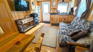 A compact living space with a wooden interior, a television mounted on the wall, a kitchenette, and a sofa with patterned cushions. - Yellowstone's Treasure Cabin #6, few min drive from Yellowstone Park (Gardiner)