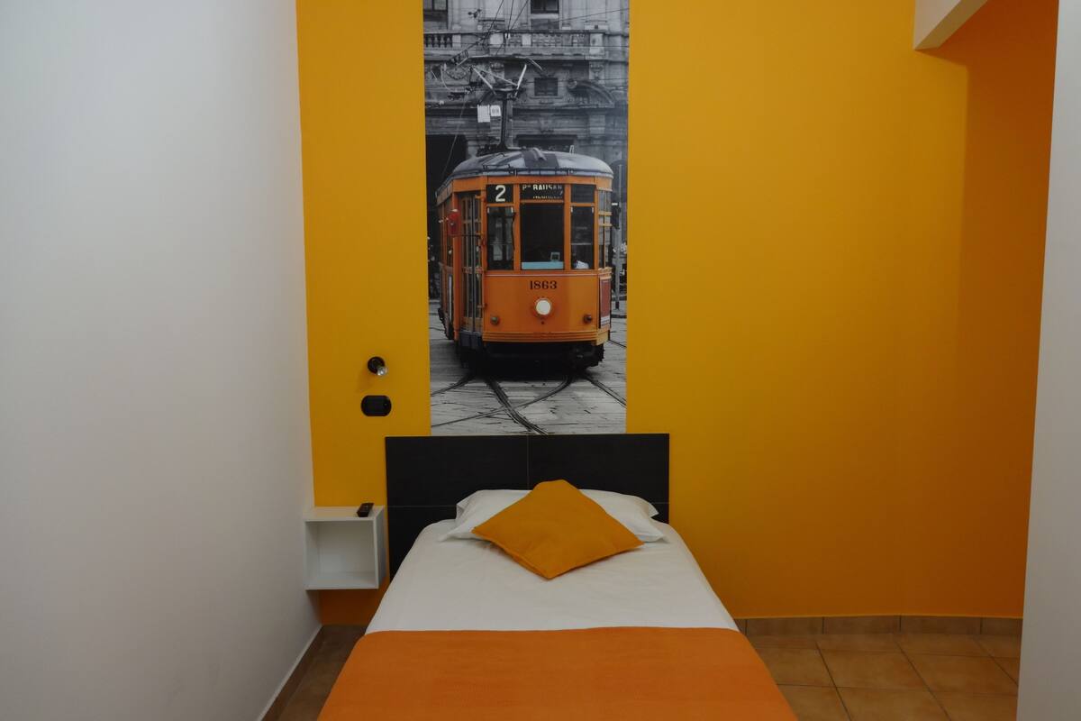 Habitación de hotel con cama, mesita de noche y un mural en la pared de un tranvía.