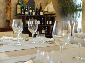 A table set with empty wine glasses and a bottle of wine, with a backdrop of wine bottles and a decorative sailboat. - Hotel Nuova Orchidea (Dresano)
