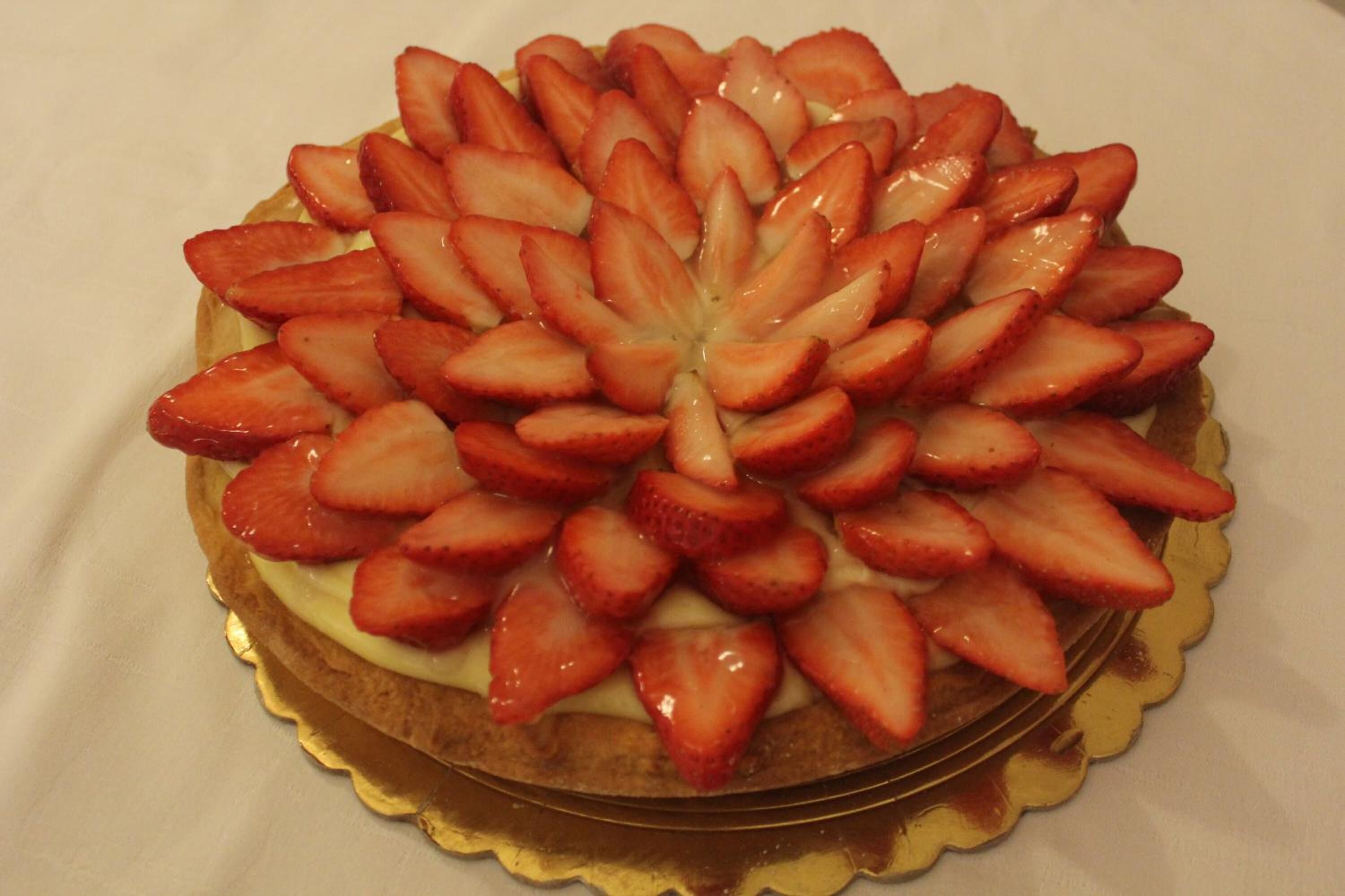 Un dessert rond, orné d’un bord doré et surmonté de tranches de fraises disposées en cercle.