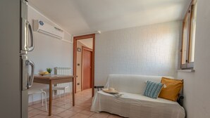 A compact room with a kitchenette, a white sofa with patterned cushions, and a brick-patterned wall.