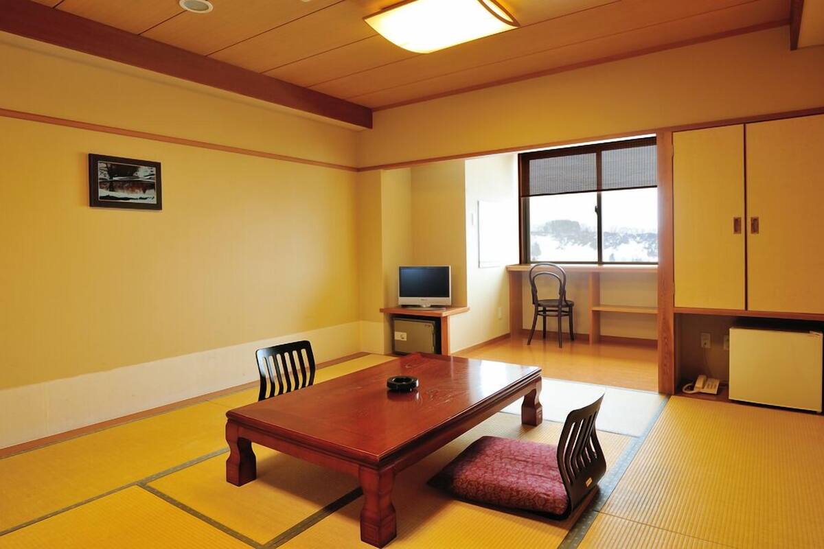 Een traditionele Japanse kamer met tatami vloerbedekking, een houten tafel, stoelen, een televisie en een raam met uitzicht.