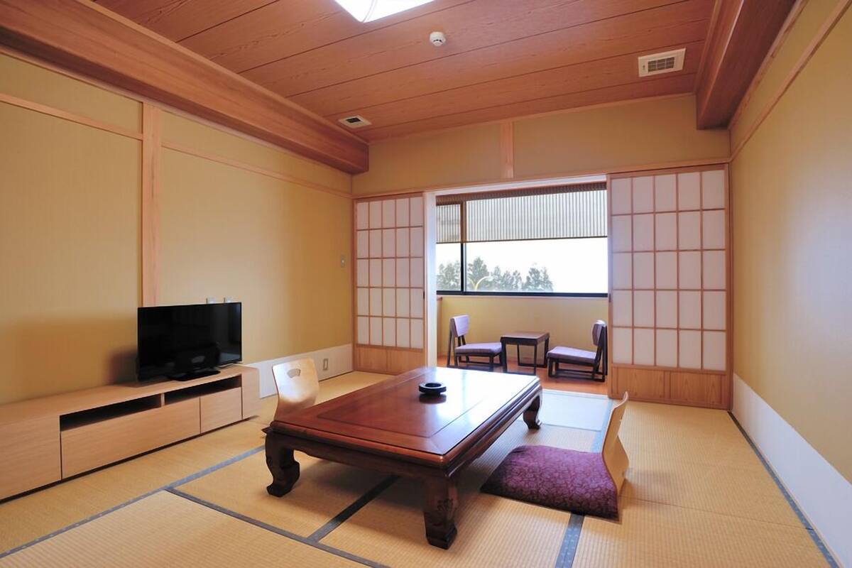 Een traditionele Japanse kamer met tatami vloerbedekking, een televisie, een lage tafel en schuifdeuren.