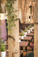Interior de restaurante com decoração em madeira de bétula, vasos brancos com plantas e mesas de madeira.