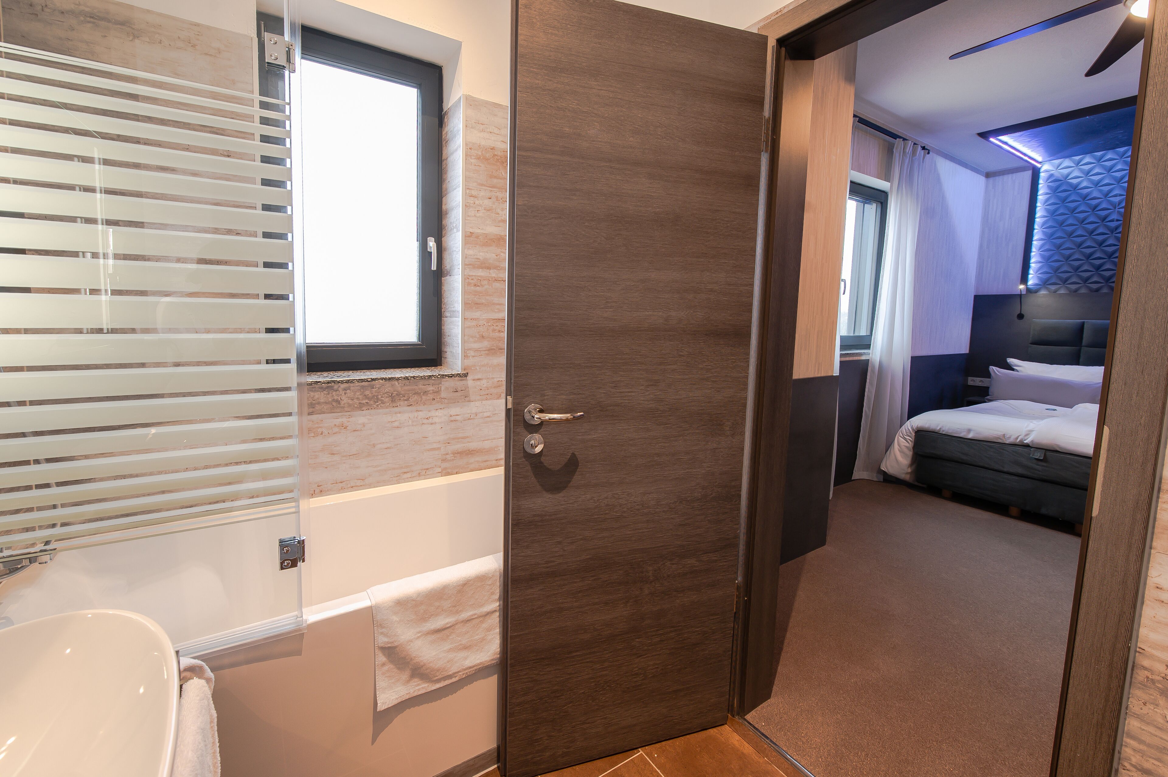 Ein modernes Badezimmer mit einer Badewanne, einer Toilette und einem Fenster mit Jalousien.