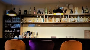 Zona de bar con tres taburetes y una estantería llena de botellas de licores.