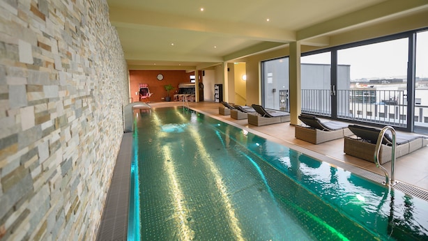 Una piscina interior con pared de piedra, sillones de descanso y vistas a la ciudad.