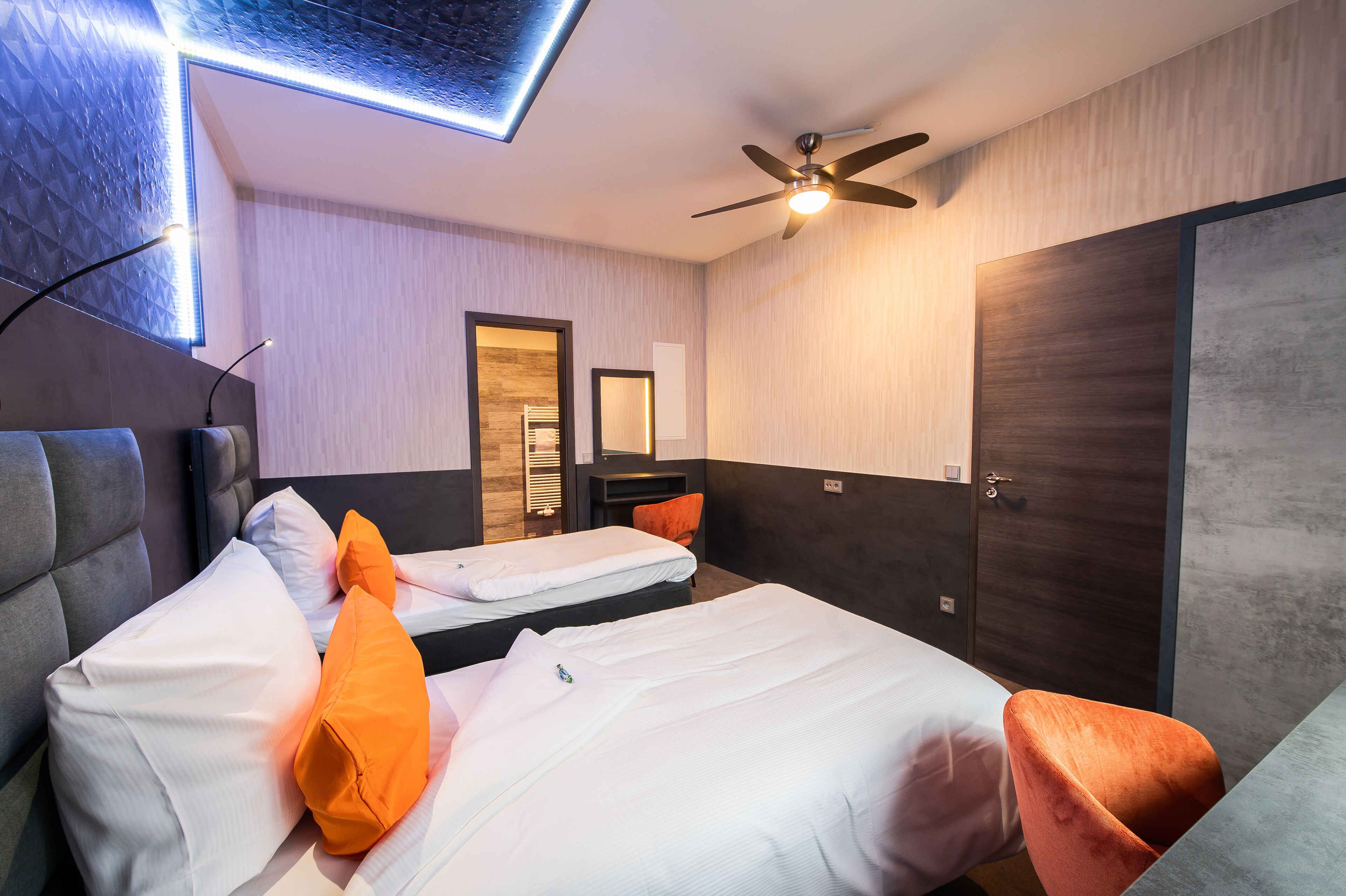 Habitación de hotel con dos camas, un ventilador de techo, un armario y una lámpara moderna.
