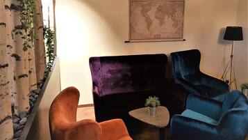 A room with a large purple sofa, a smaller orange armchair, and a blue armchair. There is a small table with a plant in the center. A world map hangs on the wall above the sofa.