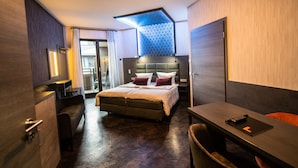 Una habitación de hotel moderna con una cama grande, un escritorio y una silla. Hay un ventilador de techo, una ventana y una puerta.