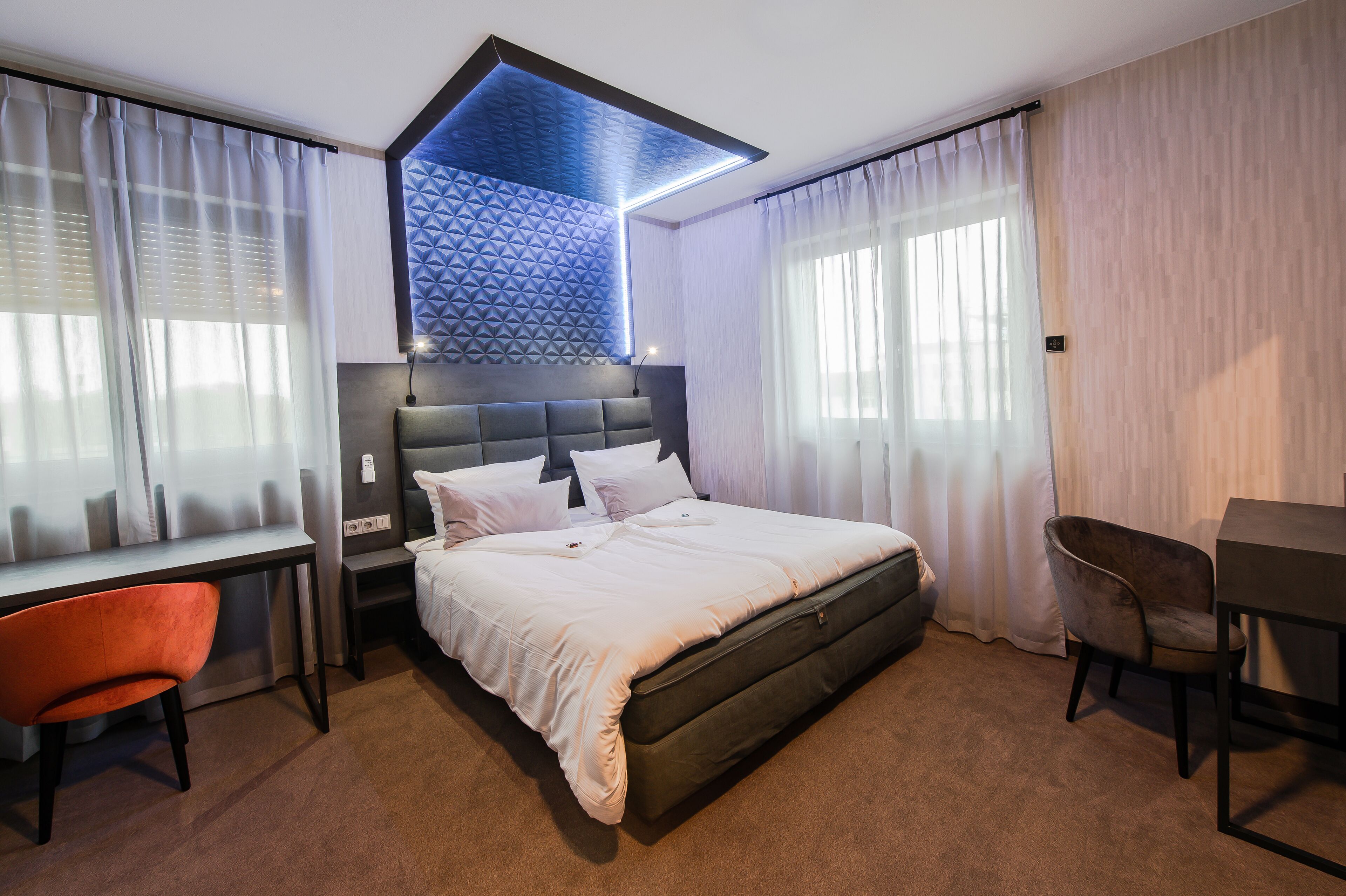 A modern hotel room with a large bed, a desk, a chair, and a small table.