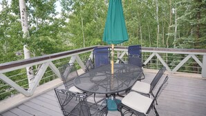 A covered outdoor deck with a round table and chairs, surrounded by a white railing, set against a backdrop of trees. - Large Family  On Adams Avenue - Ski In/out 5 Bedroom Home by RedAwning (Snowmass Village)