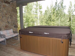 A hot tub with a wooden exterior and a brown cover, positioned on a wooden deck with a stone wall and a bench in the background. - Large Family  On Adams Avenue - Ski In/out 5 Bedroom Home by RedAwning (Snowmass Village)