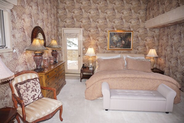 A bedroom with a large bed, two bedside tables with lamps, a chair, a dresser, and a painting on the wall.