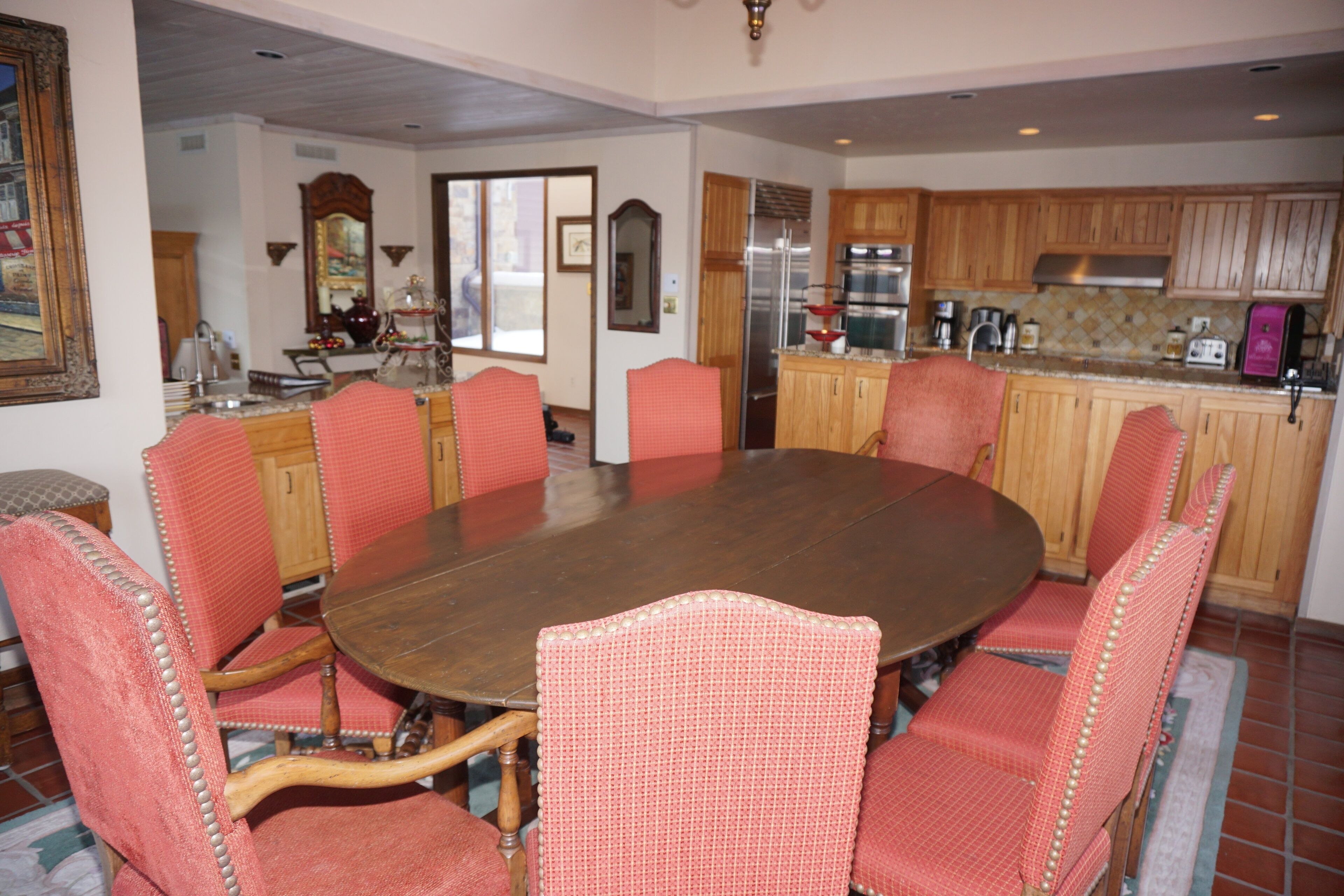A dining room with a large wooden table surrounded by six red upholstered chairs with wooden frames.