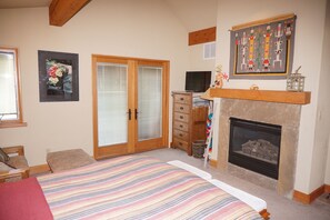 A bedroom with a large bed, a fireplace, a television, and a wooden dresser.