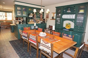 A traditional kitchen with green cabinets, a wooden dining table, and a chandelier.