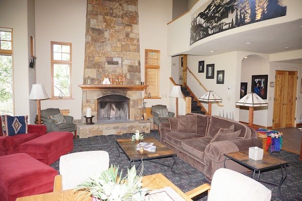 A spacious living room with a stone fireplace, red and brown sofas, and a wooden coffee table.