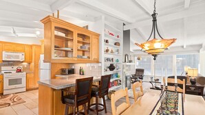 A modern kitchen with wooden cabinets, a central island with bar stools, and a dining area with a table and chairs. - Aspen West End  - Quiet Neighborhood 3 Bedroom Home by RedAwning (Aspen)
