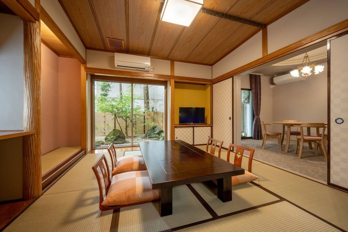 Een traditionele Japanse kamer met tatami vloerbedekking, een houten eettafel en een televisie.