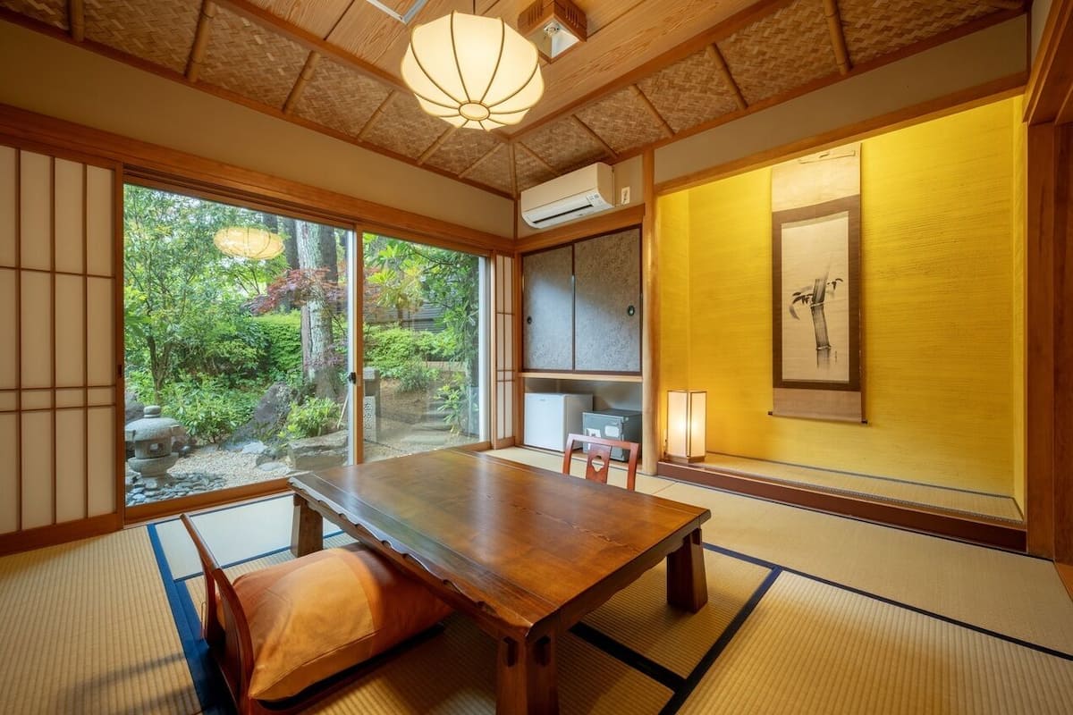 Een traditionele Japanse kamer met tatami vloeren, een houten tafel, schuifdeuren en uitzicht op een tuin.