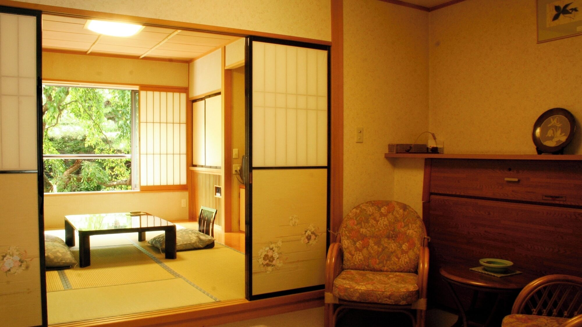 Una habitación japonesa tradicional con suelo de tatami, un divisor corredizo shoji, una mesa baja con cojín y una silla con estampado floral.