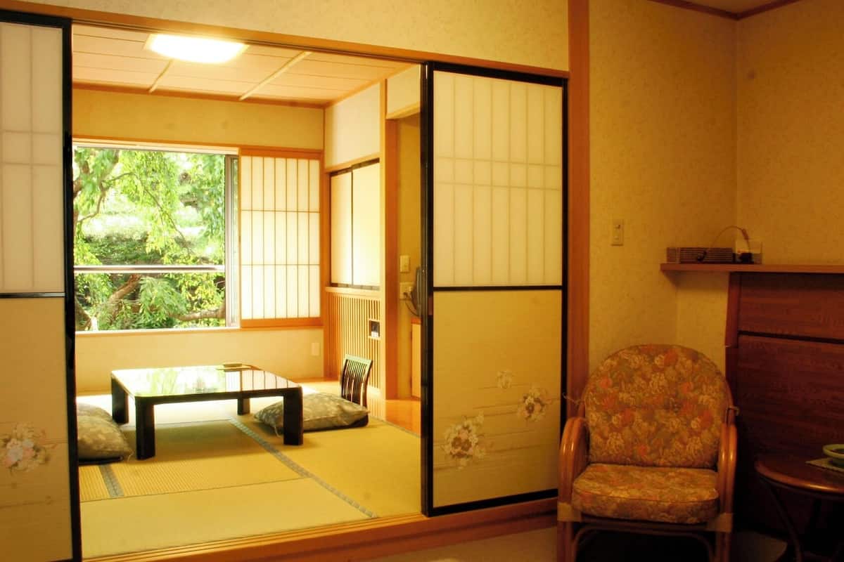 A traditional Japanese room with tatami flooring, a sliding shoji screen, a low table with a cushion, and a chair with a floral pattern.