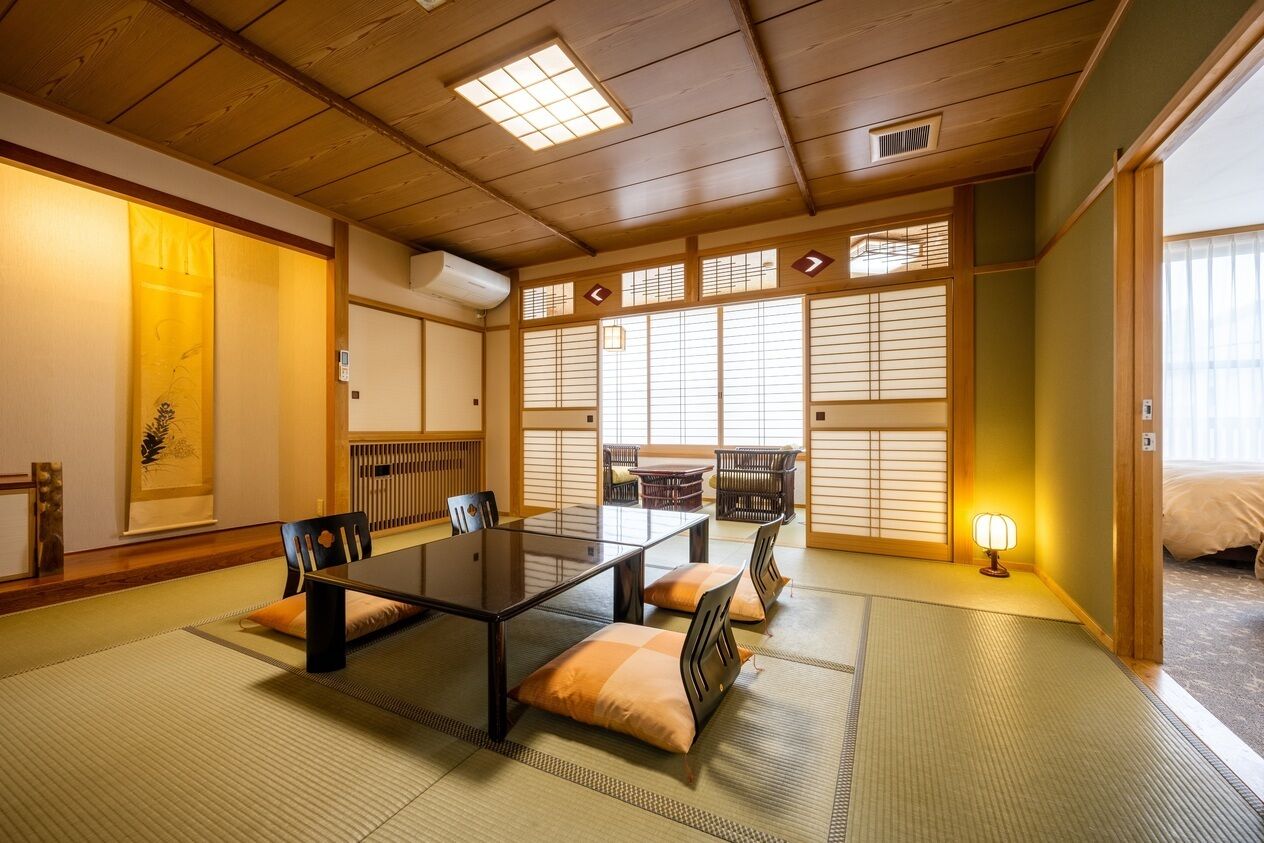 Una habitación japonesa tradicional con suelo de tatami, una mesita baja, sillas y puertas correderas.