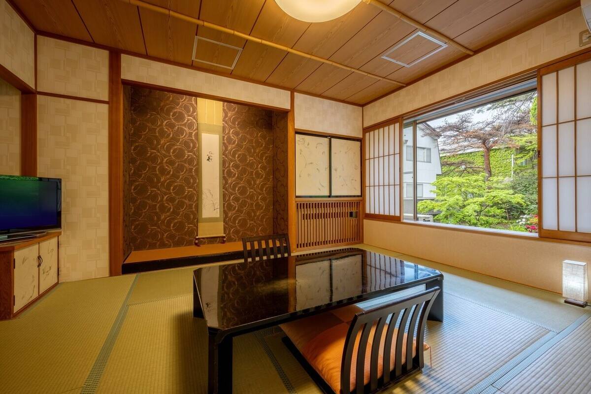 Een traditionele Japanse kamer met tatami vloeren, een lage tafel, schuifdeuren en uitzicht op groen.