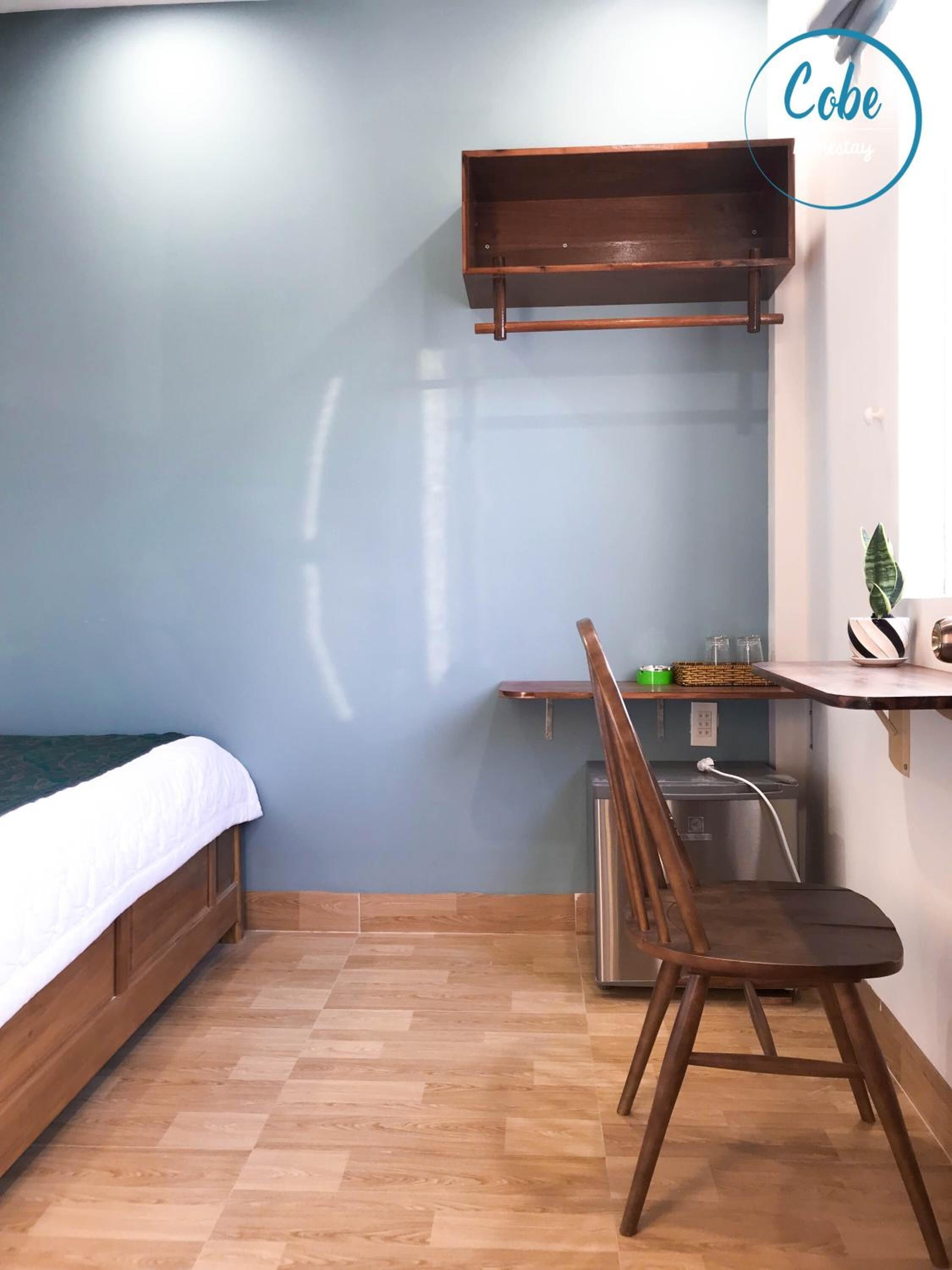 A compact room with a bed, a desk, a chair, and a small kitchenette.