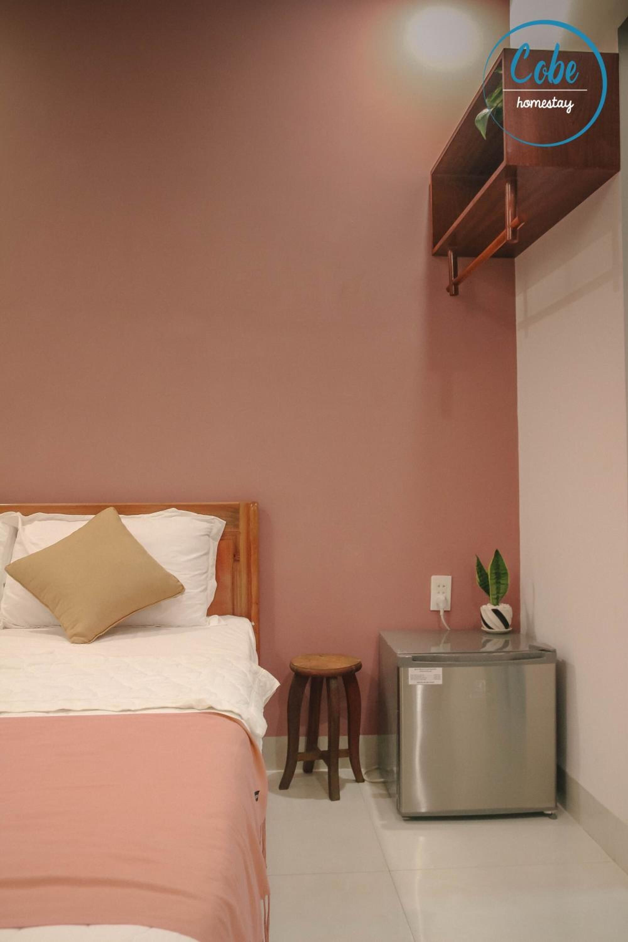 A bedroom with a bed, a small stool, and a refrigerator.