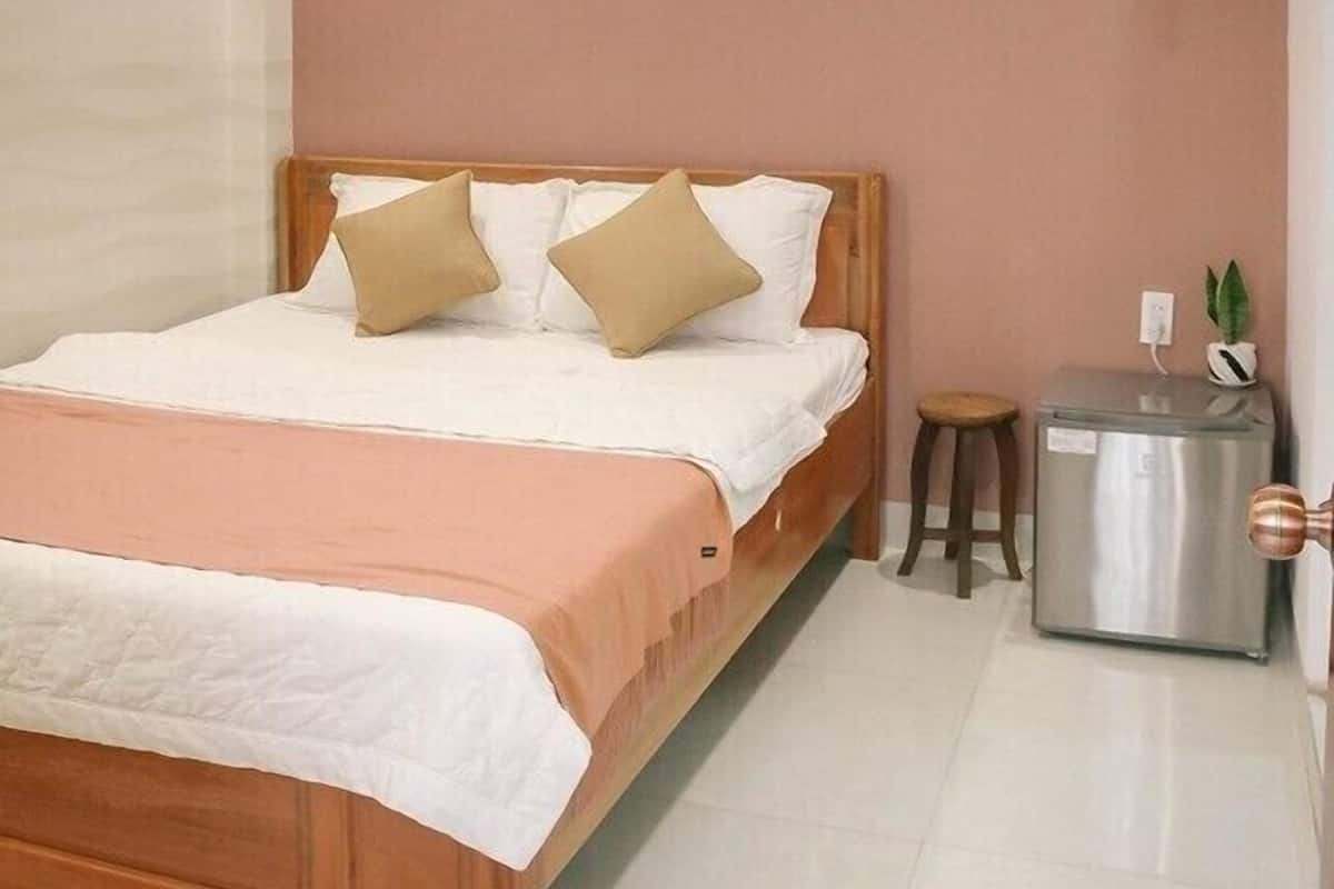 A bedroom with a wooden bed, white bedding, a small stool, and a metallic object on the floor.