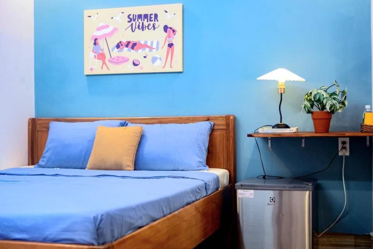A bedroom with a bed, a nightstand, a lamp, a potted plant, and a wall art piece.