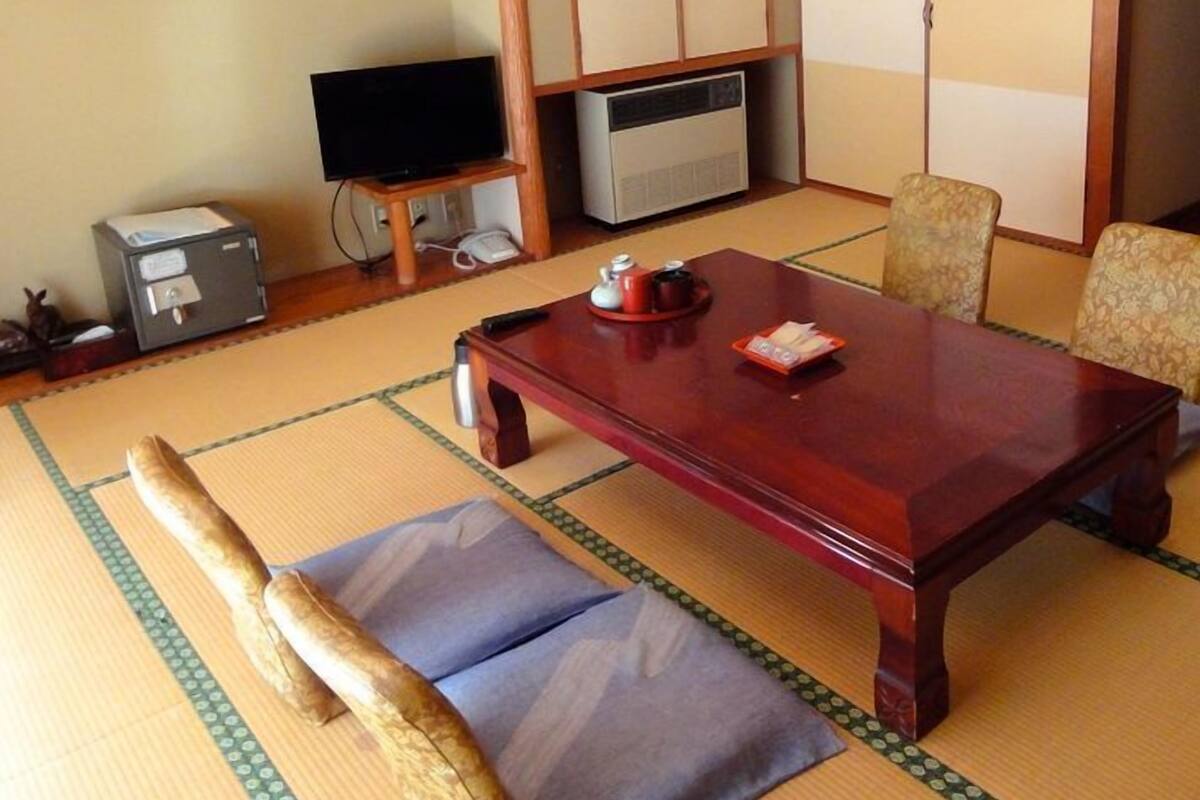 A traditional Japanese-style room with tatami flooring, a low wooden table, a television, and a cabinet.