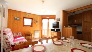 A dining area with a table set for four, wooden walls, a television on a stand, and a kitchen area with wooden cabinets. - Ground floor, balcony, tv, ski locker, 43m², Val Cenis (Lanslevillard)